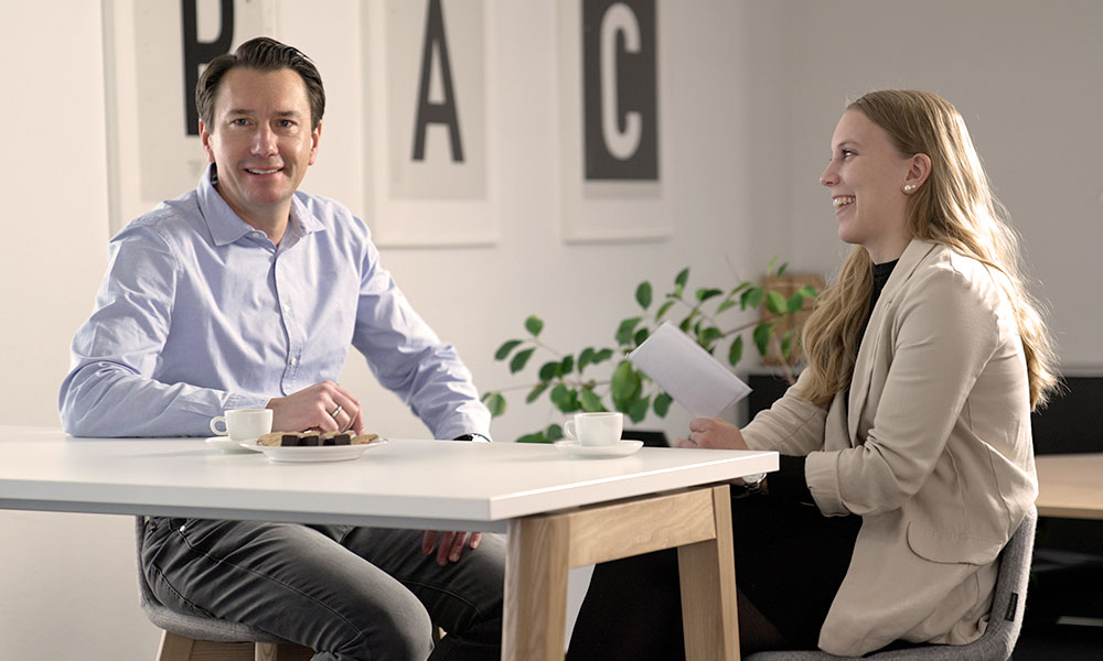 PAC Geschäftsführer Martin Jünger im Interview mit Hannah Reith am Tisch sitzend mit Espressotassen und Gebäck.